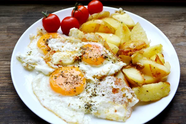 Grote ronde plaat vol met gebakken eieren, patat en cherry tomaten - een traditionele continentaal ontbijt — Stockfoto