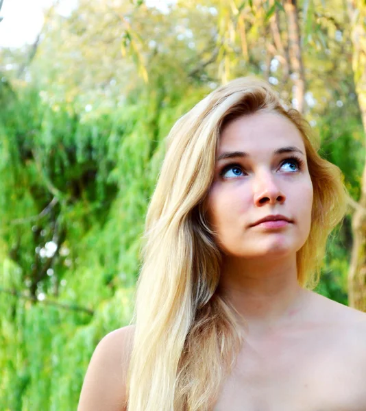 年轻漂亮的金发女郎，用长长的头发，视线和绿色森林里轻轻地微笑 — 图库照片