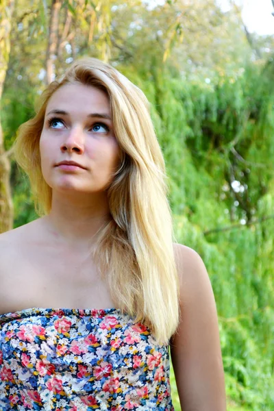 Junge schöne blonde Frau mit langen Haaren, die wegschaut und sanft im grünen Wald lächelt — Stockfoto