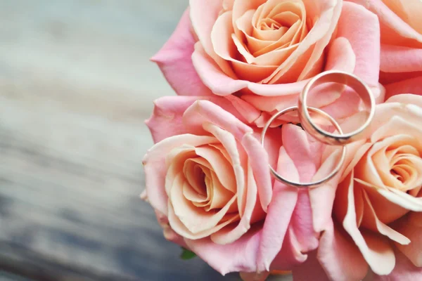 Due anelli d'oro di fidanzamento su un bellissimo bouquet da sposa di rose rosa — Foto Stock