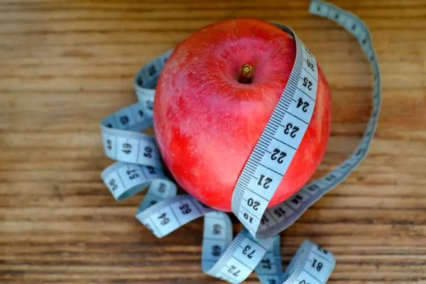 Диетическая концепция с красным яблоком и синей измерительной лентой на деревянном столе — стоковое фото