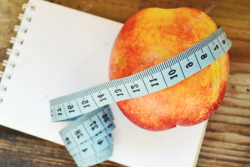 Diet concept with red apple, a notebook and blue measuring tape on wooden table