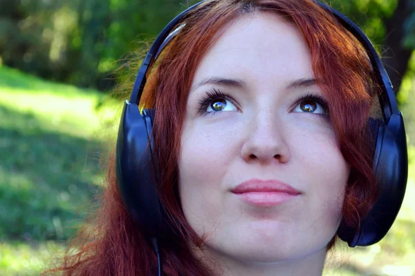 Vakker, rødhåret kvinne i store hodetelefoner som hører på musikk med et lykkelig smil – stockfoto