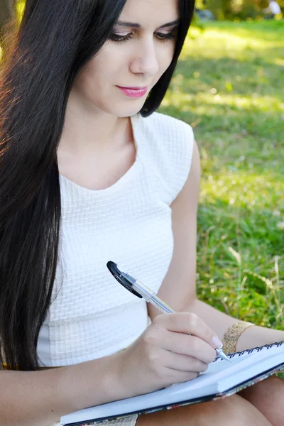 Jeune femme brune avec de belles mains écrivant dans son journal intime et souriant — Photo