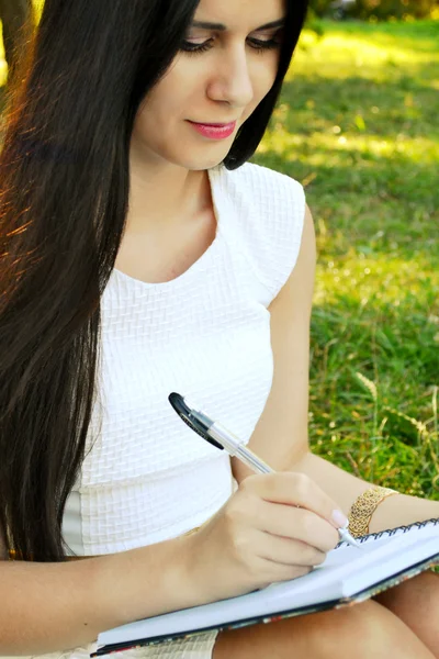 Młoda brunetka kobieta z piękne dłonie, pisząc w swoim pamiętniku i uśmiechając się — Zdjęcie stockowe