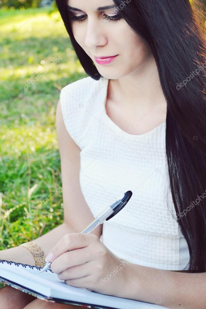 Young brunette woman with beautiful hands writing in her diary and smiling