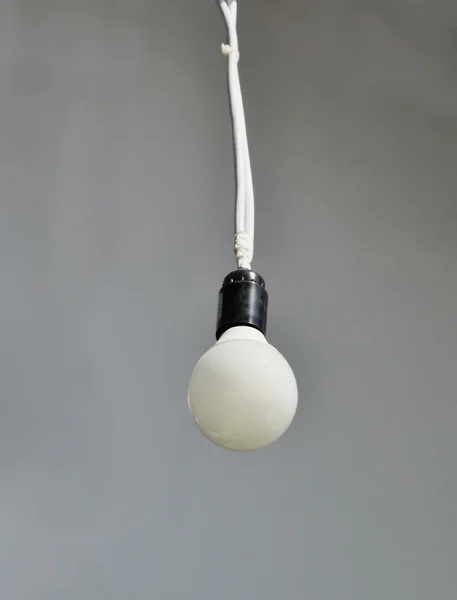 Lampadina bianca solitaria appesa al soffitto su sfondo grigio — Foto Stock