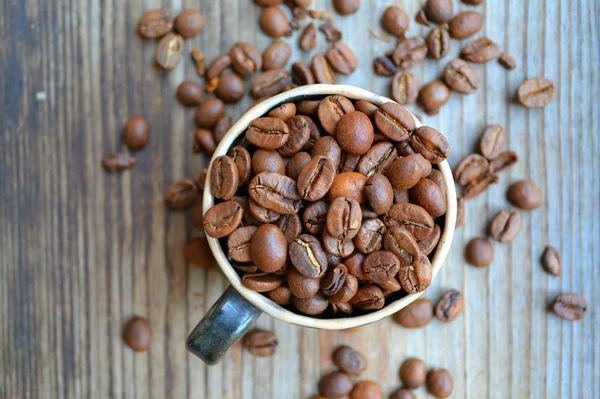 Cup full of coffee beans on wooden table — Stock Photo, Image