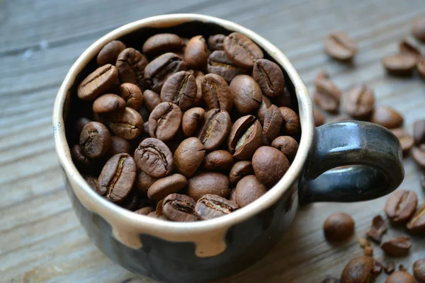 Cup full of coffee beans on wooden table — Stock Photo, Image