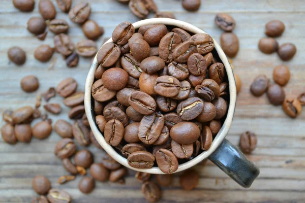 Cup full of coffee beans on wooden table — Stock Photo, Image