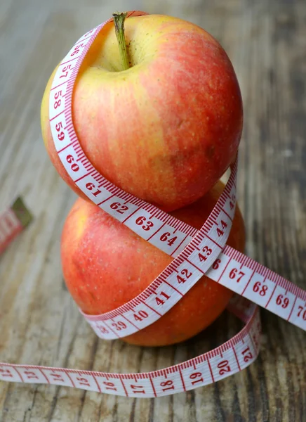 Conceito de dieta com maçãs vermelhas e amarelas e fita métrica branca na mesa de madeira — Fotografia de Stock