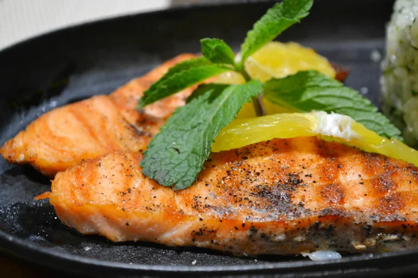 Dos filetes de salmón a la parrilla con limón y hierba de menta en plato negro —  Fotos de Stock