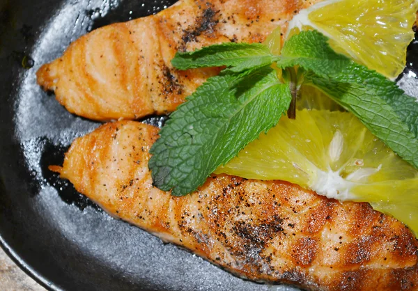Two grilled salmon steaks with lemon and mint herb on black plate — Stock Photo, Image