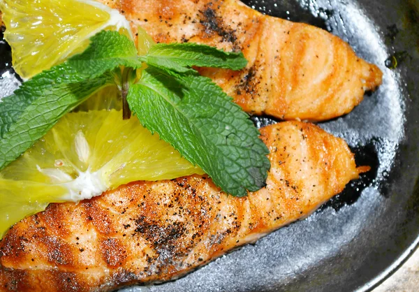 Two grilled salmon steaks with lemon and mint herb on black plate — Stock Photo, Image