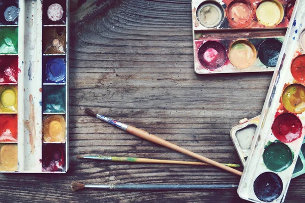 Colorful paints and brushes arranged as a frame on wooden table — Stock Photo, Image