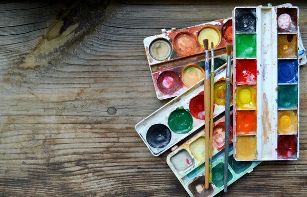 Colorful paints and brushes arranged as a frame on wooden table — Stock Photo, Image