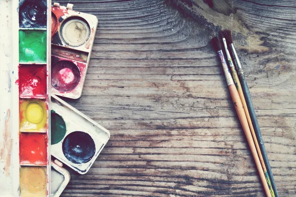 Colorful paints and brushes arranged as a frame on wooden table — Stock Photo, Image