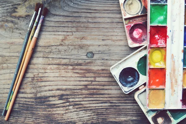Colorful paints and brushes arranged as a frame on wooden table — Stock Photo, Image