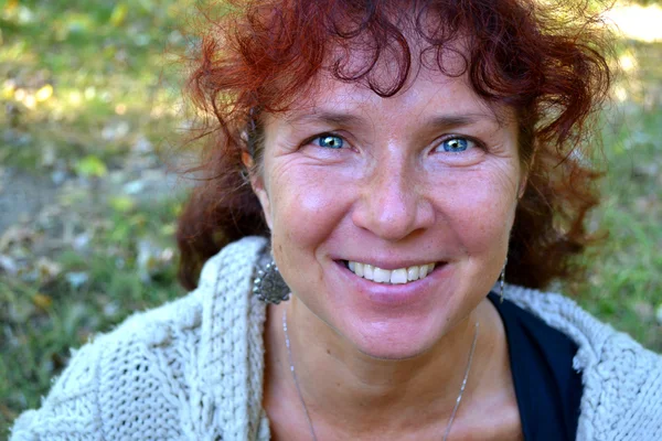 Mujer hermosa feliz con el pelo rojo en sus cuarentas oliendo al aire libre — Foto de Stock