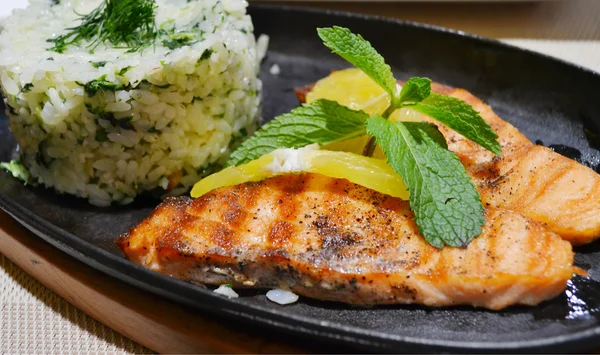 Two grilled salmon steaks with rice, lemon and mint herb on black plate — Stock Photo, Image