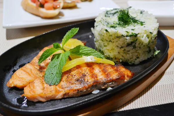 Two grilled salmon steaks with rice, lemon and mint herb on black plate — Stock Photo, Image