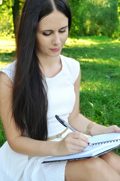 Young brunette woman with beautiful hands writing in her diary and smiling — Stock Photo, Image