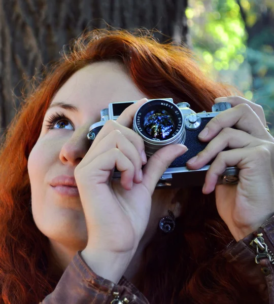 Молода руда жінка з ретро камерою фотографує — стокове фото