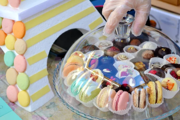 Mão segurando tampa bandeja sobre macarons coloridos (amarelo, rosa, laranja) em um prato com doces de chocolate — Fotografia de Stock