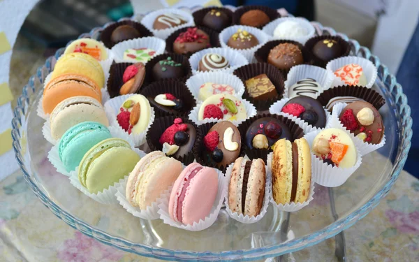 Colorful (yellow, pink, orange) macarons on a plate with chocolate candies — Stock Photo, Image