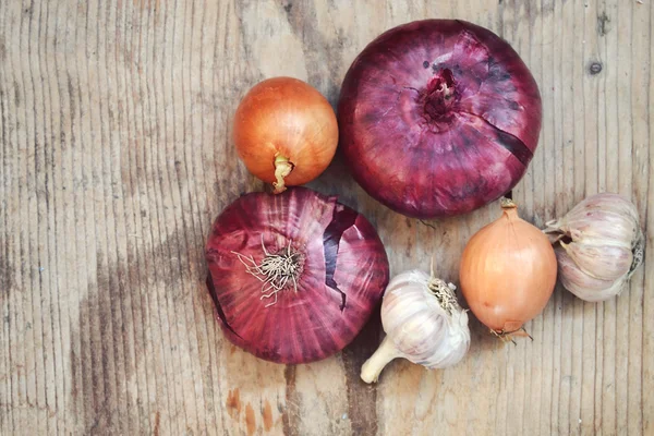 Red and bulb onions with whole organic garlic on wooden table — Stock Photo, Image