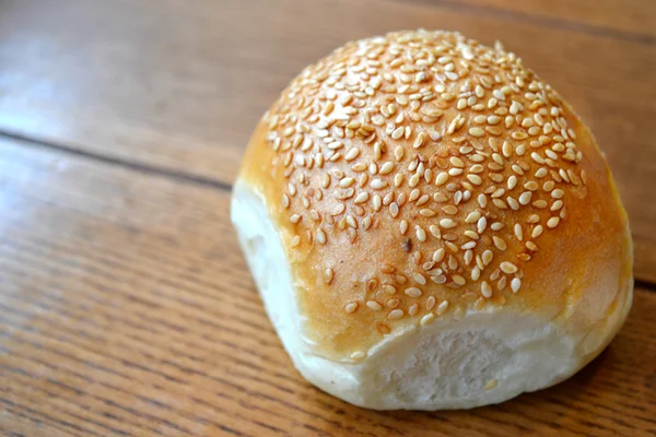 Leckeres Brötchen mit Sesam auf Holztisch — Stockfoto