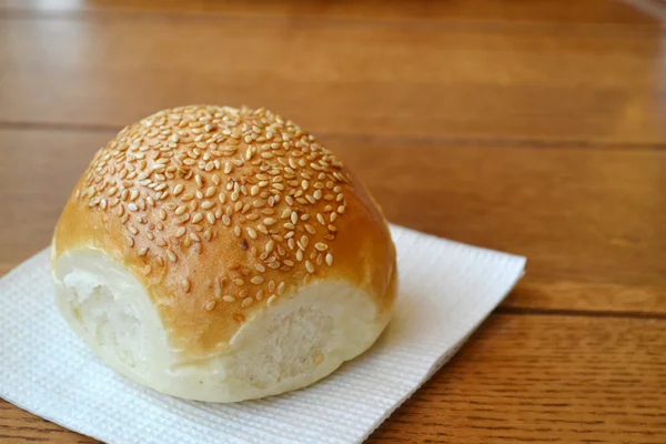 Sabroso bollo con semillas de sésamo en mesa de madera —  Fotos de Stock