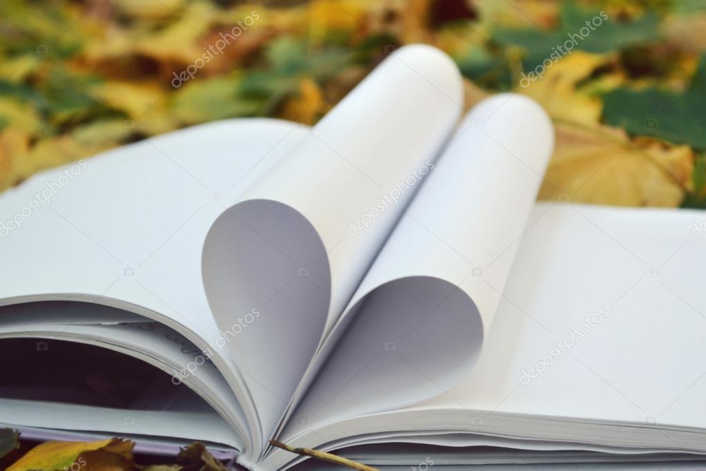 Book pages curved into a shape of heart covered with autumn leaves