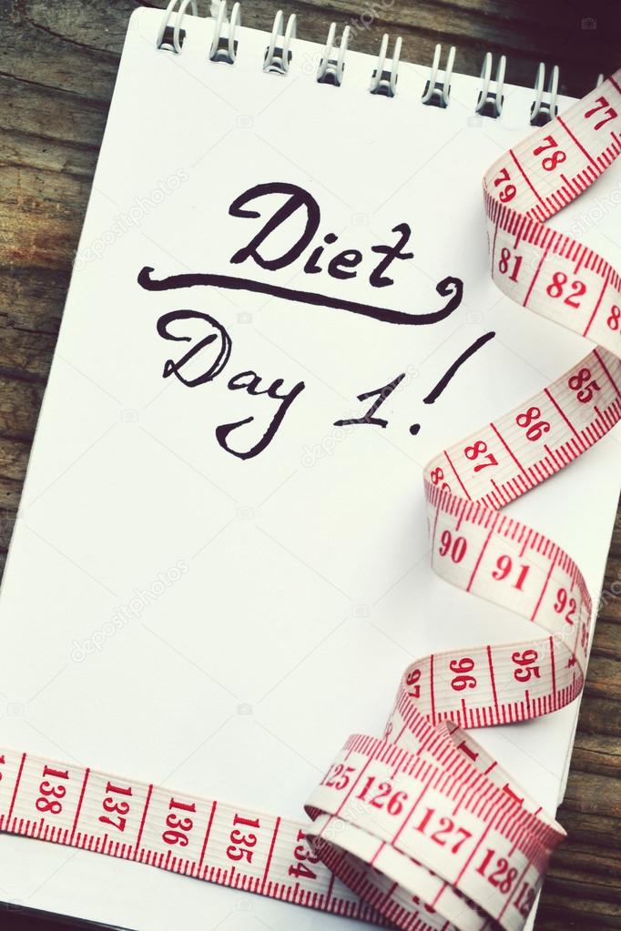 Diet concept with a notebook and red measuring tape on wooden table