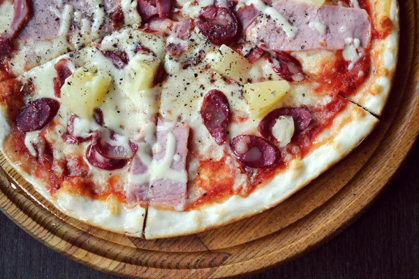 Round pizza with sausages and pineapple on a wooden plate — Stock Photo, Image