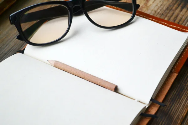 An empty retro notebook with old paper, little pencil, glasses and leather cover — Stock Photo, Image