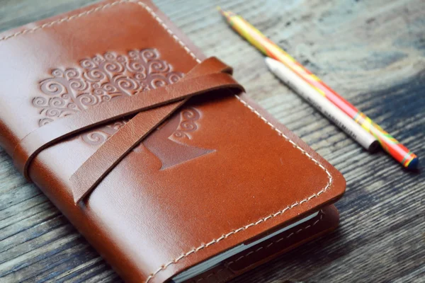 Un viejo cuaderno en funda de cuero con lápices sobre mesa de madera — Foto de Stock