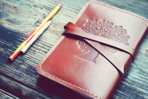 Starý notebook v kožený obal s tužky na dřevěný stůl — Stock fotografie
