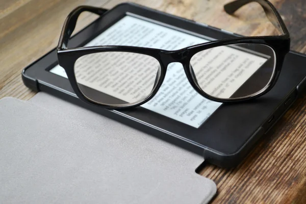 Black ereader with retro glasses on wooden table — Stock Photo, Image