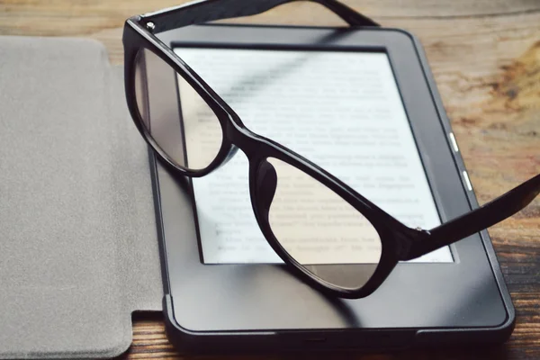 Black ereader with retro glasses on wooden table — Stock Photo, Image