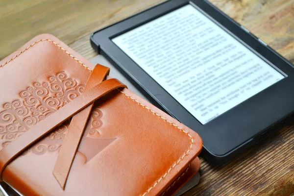 Ahşap masa üzerinde deri kapağı içinde yaşlı bir defter ile siyah ereader