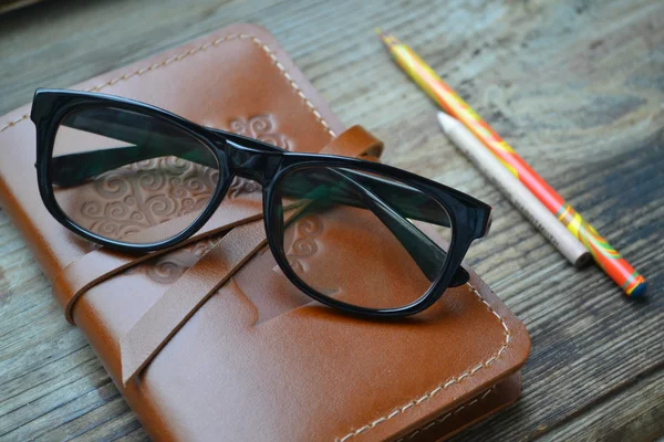 Un vieux carnet en cuir recouvert de crayons et de verres sur table en bois — Photo