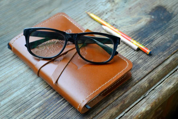 Ein altes Notizbuch in Ledereinband mit Bleistiften und Gläsern auf Holztisch — Stockfoto