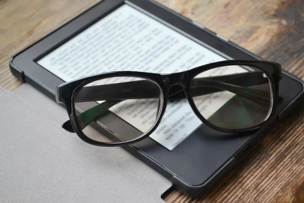 Black ereader with retro glasses on wooden table — Stock Photo, Image