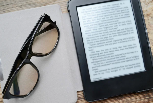 Black ereader with retro glasses on wooden table — Stock Photo, Image