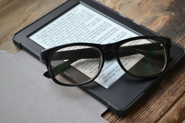 Black ereader with retro glasses on wooden table