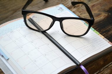 An empty retro daily planner with black pencil and reading glasses clipart