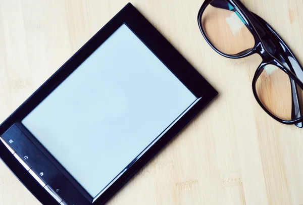 KYIV, UKRAINE - JANUARY 25, 2015: Black ereader with reading glasses on wooden table — Stock Photo, Image