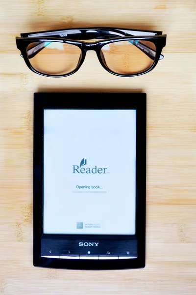 KYIV, UKRAINE - JANUARY 25, 2015: Black Sony ereader with reading glasses on wooden table — Stock Photo, Image