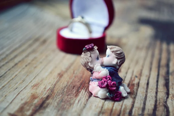 Red heart shaped ring box with platinum engagement ring and a pair of lovers on wooden table — Stock Photo, Image